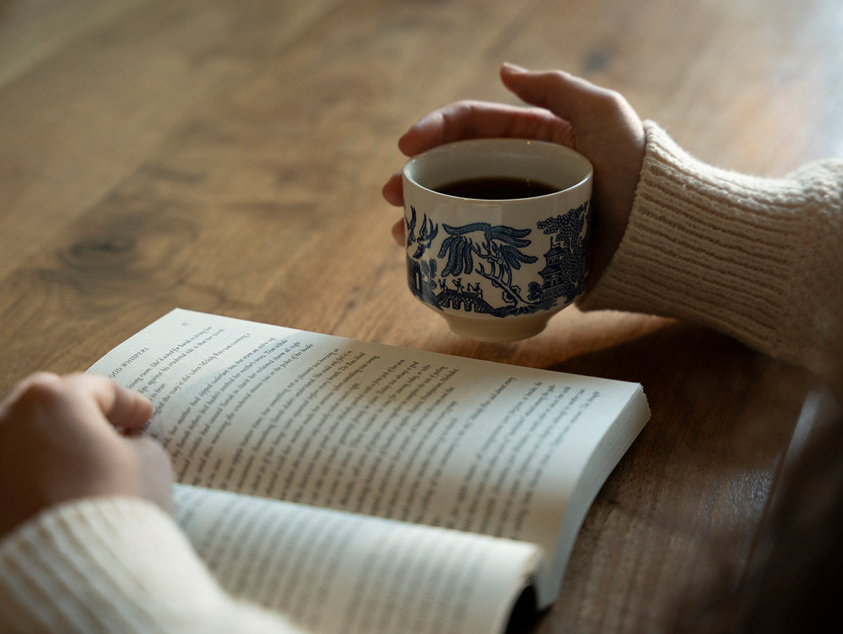 Person holding a cup of coffee while reading a book